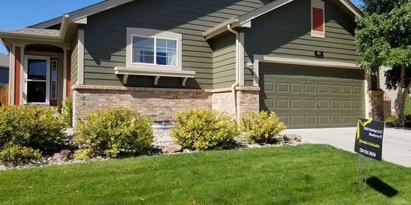 Modern single-story house with green siding and brick accents under a clear blue sky.