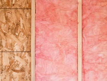 Pink fiberglass insulation between wooden wall studs.