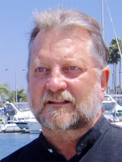 headshot of author AFN Clarke, blue eyes, moustache, short greying hair, black shirt, in sunshine