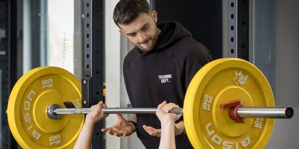 A man bench pressing weights with a trainer spotting him.