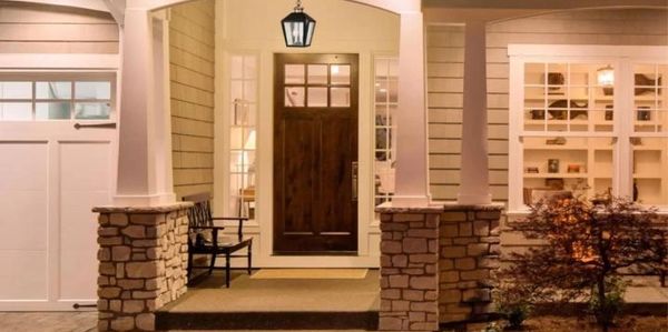 Warmly lit front porch with stone pillars and wooden door at night.