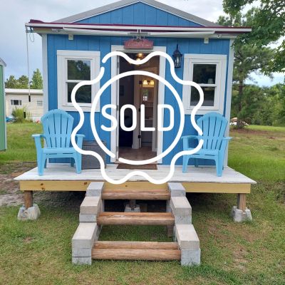 Tiny blue house with porch and chairs marked sold.
