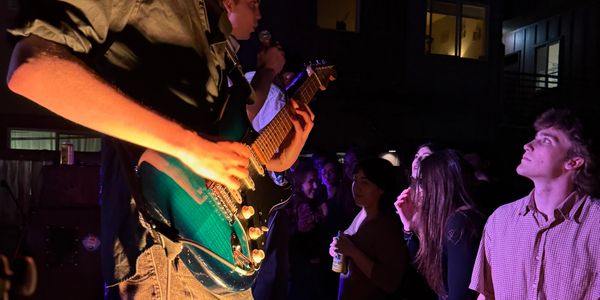 A blue electric guitar player performs on stage with an attentive crowd.