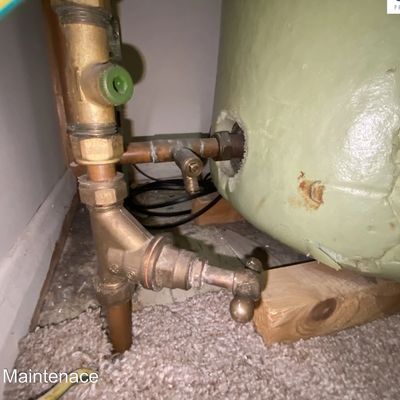 Old plumbing pipes with a valve near a water heater.