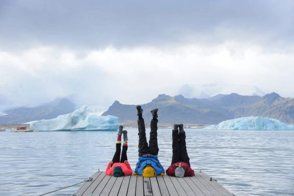 Three people doing headstands on a dock with icebergs and mountains in the background.