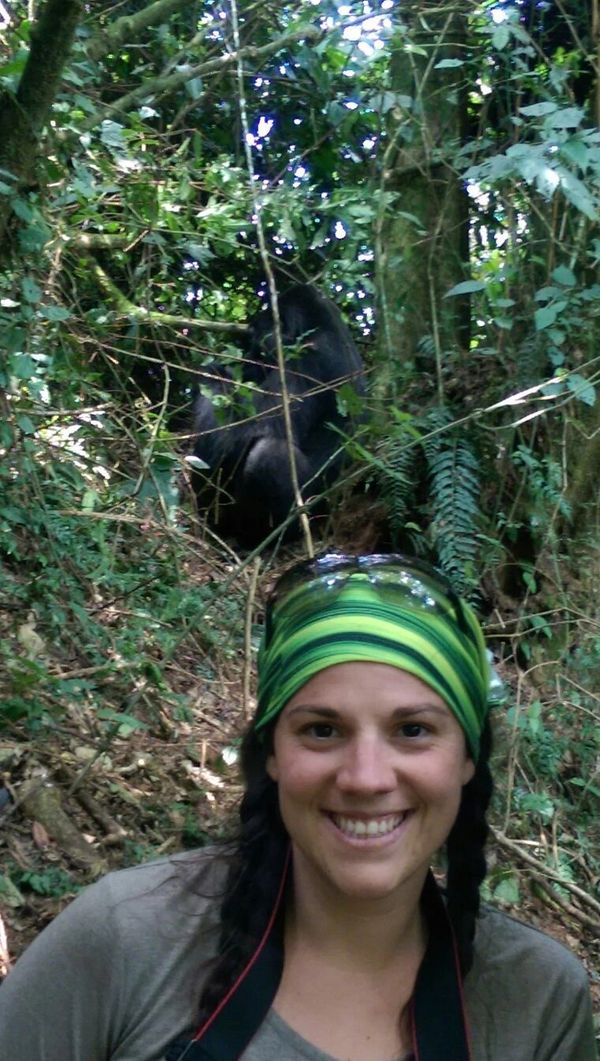 Smiling woman in a green headband with a gorilla in the forest behind her.