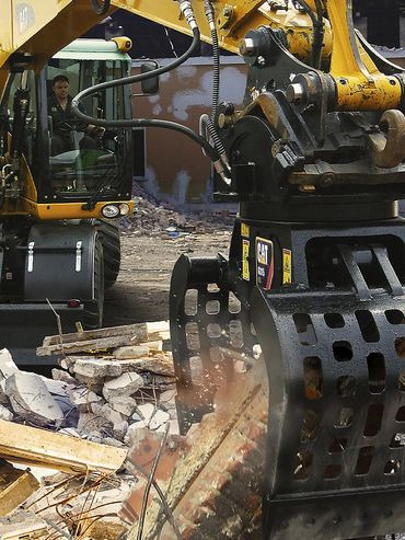 Yellow excavator demolishing a building amid rubble and debris.