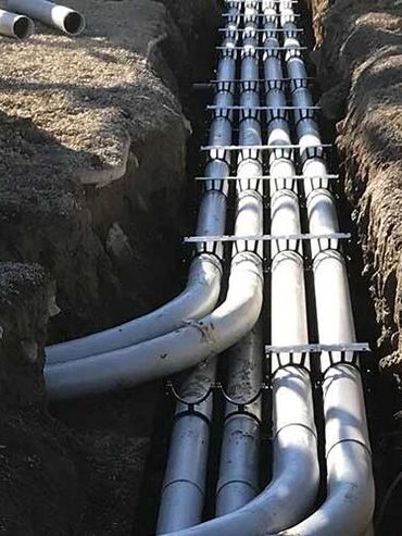 Multiple large metal pipes installed in a trench underground.