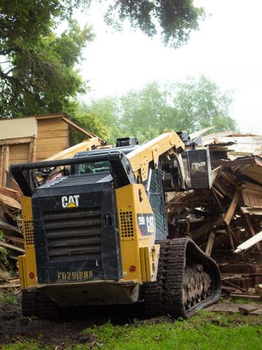 A bulldozer demolishing a wooden house surrounded by trees.