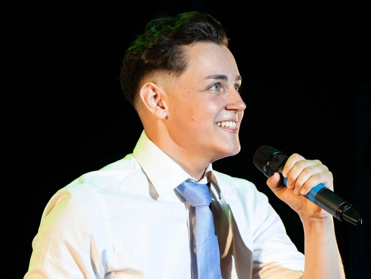 Man in white shirt and blue tie holding a microphone.