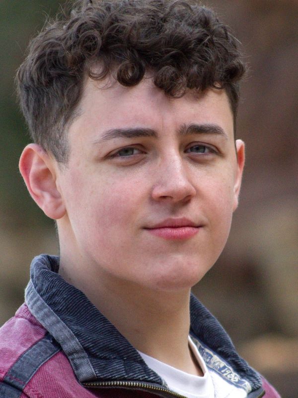 Young man with curly hair wearing a red and gray jacket.