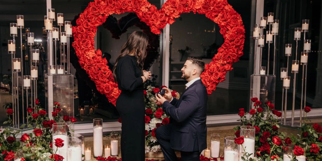 Man proposing to woman with red rose heart and candles.