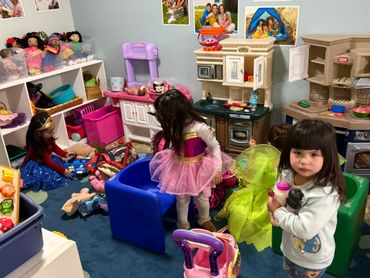 Children playing in a colorful, toy-filled playroom with family photos on the wall.