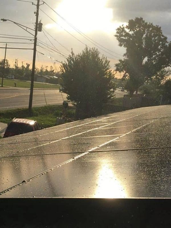 Sunlight reflecting on rain-speckled solar panels on a rooftop at sunset.