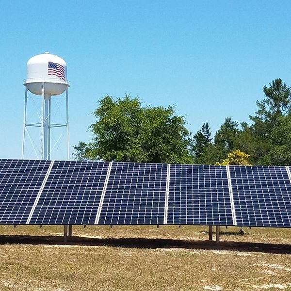 Solar panels in a field with a water tower in the background.