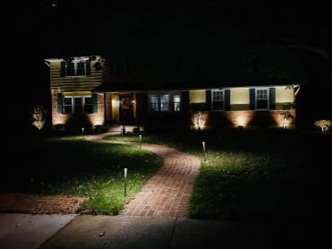 Lit brick pathway leading to a house at night.