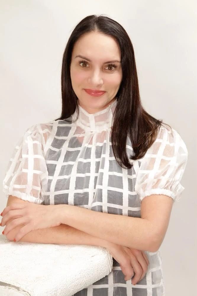 Woman with long dark hair in a white checkered blouse, smiling gently.