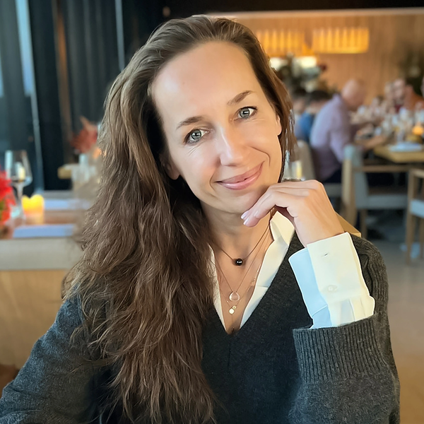 Smiling woman with wavy brown hair wearing a white blazer and shirt.