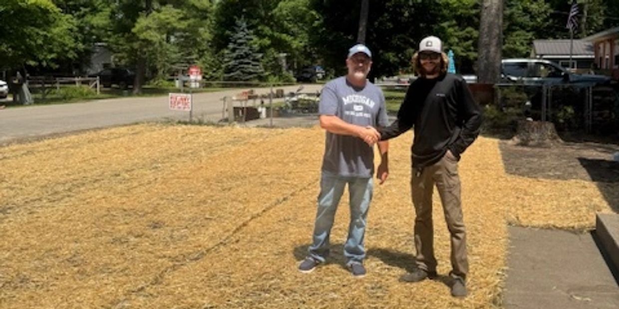 Two men shaking hands on a newly seeded yard covered with straw.