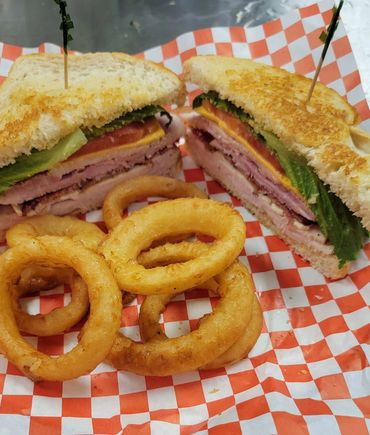 A club sandwich cut in half seven with golden onion rings.