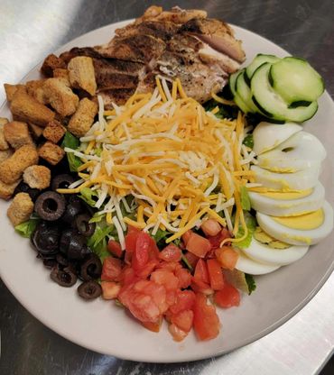 A plate of lettuce covered with tomatoes, olives, cheese, croutons, chicken, cucumbers, and an egg.