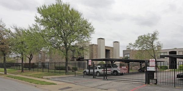 Gated apartment complex with tall trees and overcast sky.