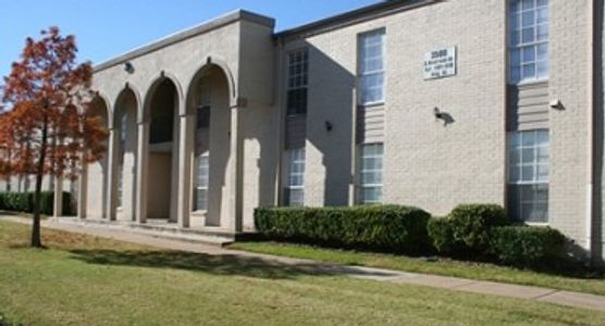 Exterior of a beige brick building with arches and neatly trimmed bushes.