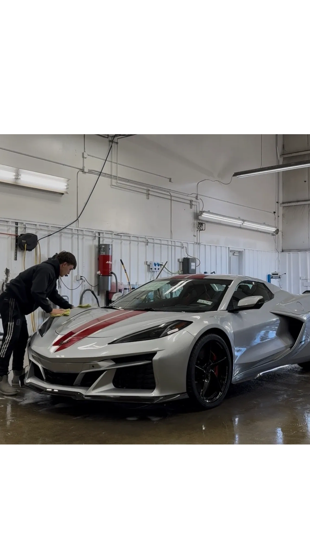Person polishing a sleek silver sports car with red racing stripes indoors.
