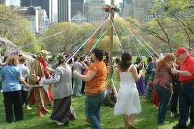 People celebrating Beltaine on May 1, dancing around the Maypole, weaving magical ribbons together.