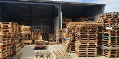 Stacks of wooden pallets stored in a warehouse under a partly cloudy sky.