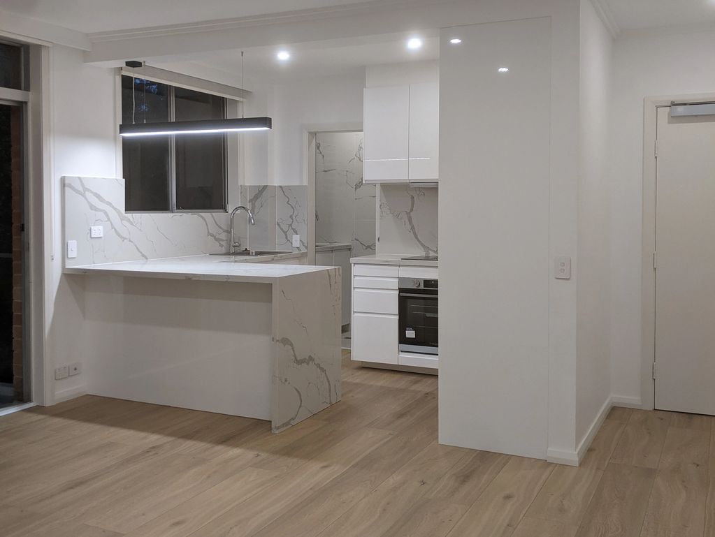 A modern open plan kitchen renovation in small apartment with waterfall white stone benchtop