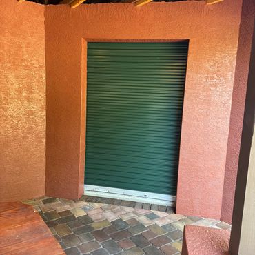 Green roll-up door in a covered patio with red textured walls and brick flooring.
