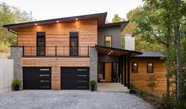 Modern wooden house with black accents and stone pillars.