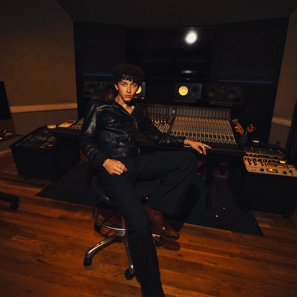 Person in a leather jacket sitting confidently in a music studio.