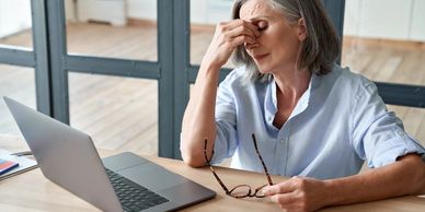 An older woman looks tense, holding her forehead, while sitting in front of a laptop.