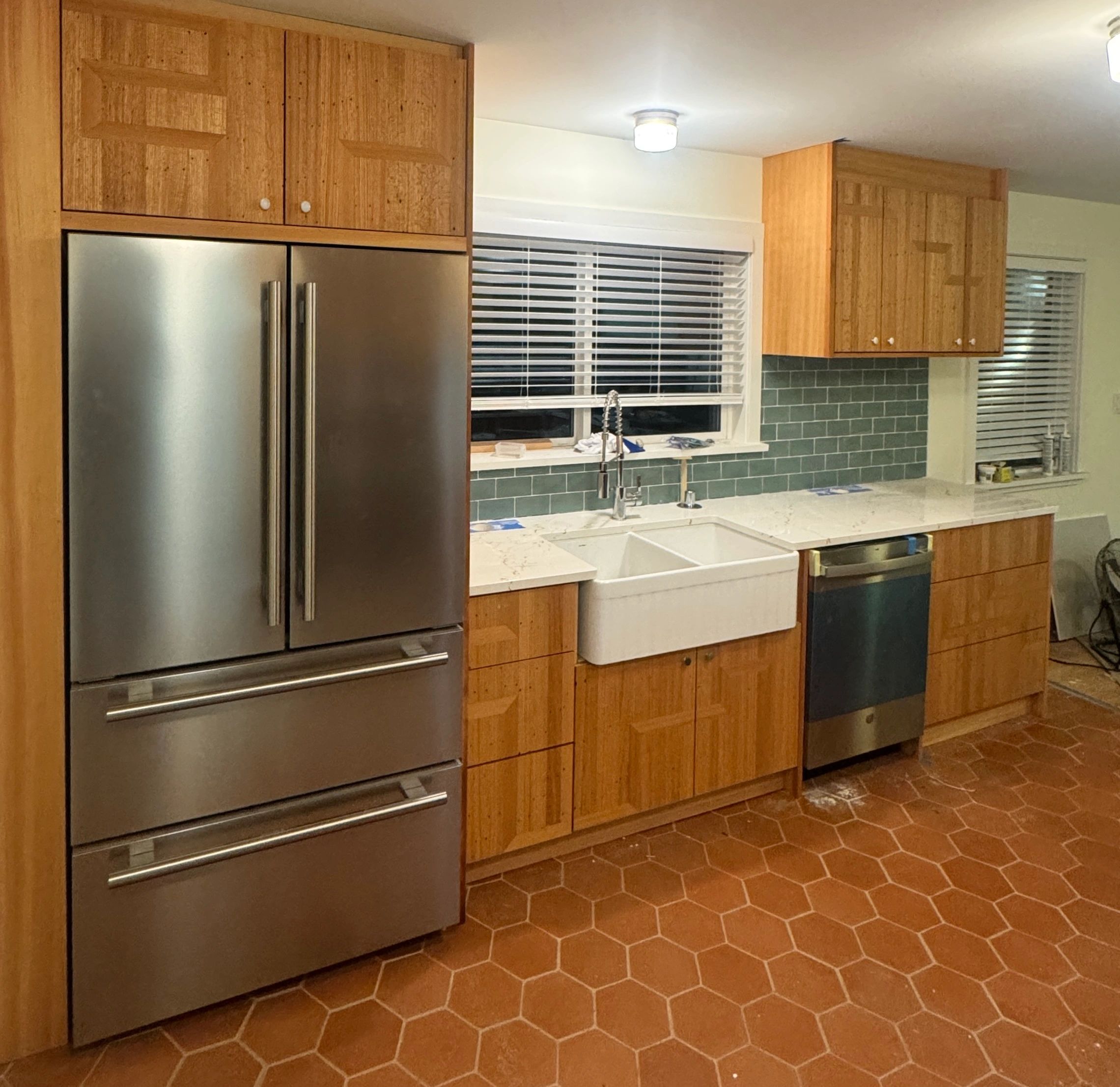 Modern kitchen with stainless steel appliances, wooden cabinets, and hexagonal terracotta floor tiles.