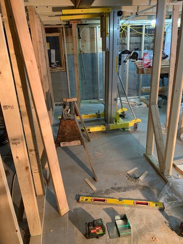 Construction site with wooden beams, tools, and a laser level in a basement area.
