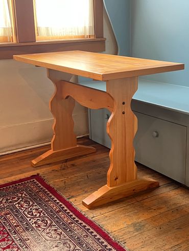 Wooden table with carved legs near a window and patterned rug on wooden floor.