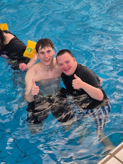 Two young men happily giving thumbs up in a swimming pool.