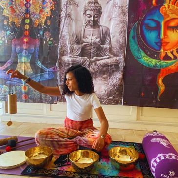 Femme assise en position de yoga avec bols chantants et décor spirituel.