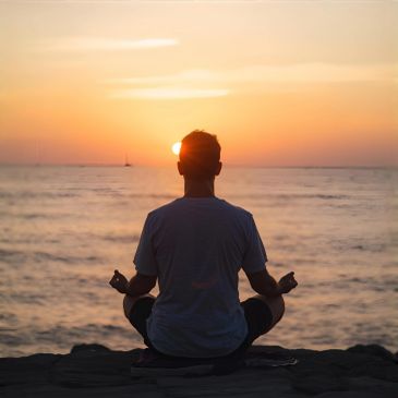 Personne méditant au coucher du soleil au bord de la mer.