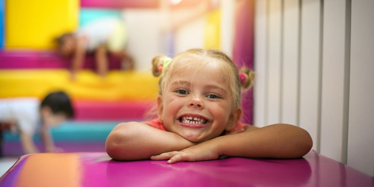 A four year old blonde girl with pig tails, folds her arms and smiles at a children's center.