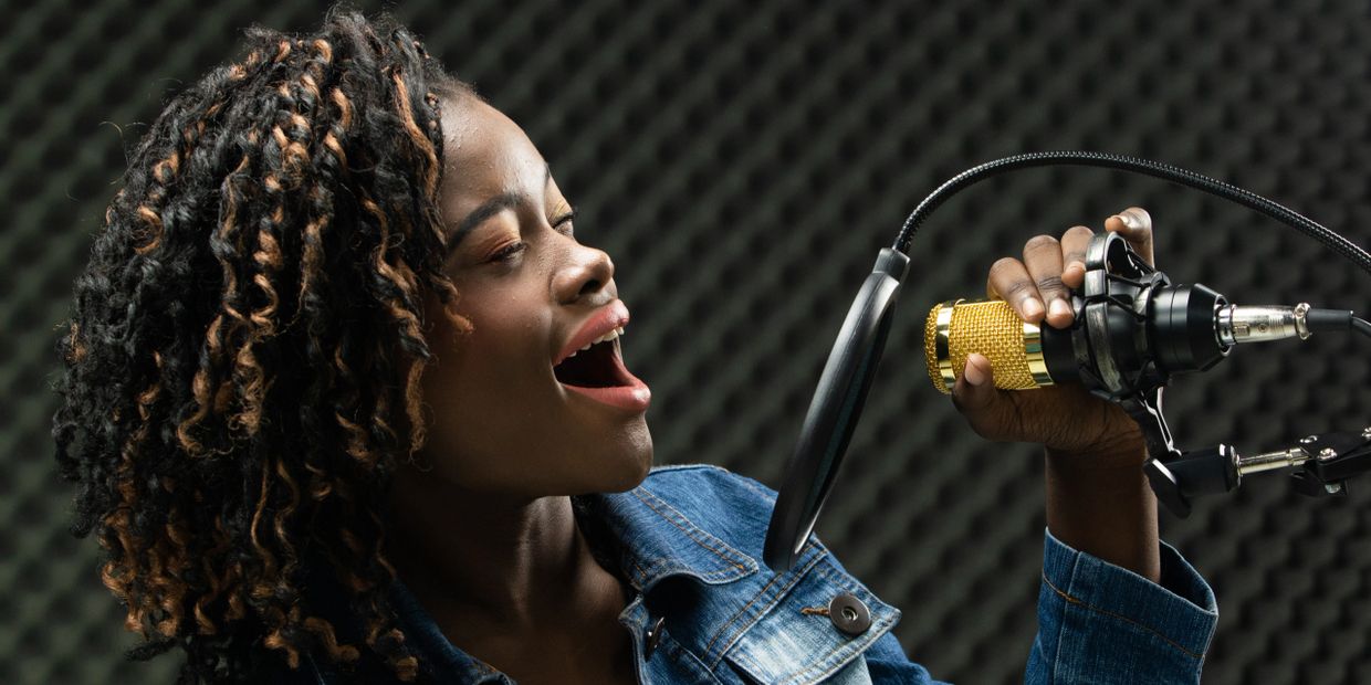 A teenaged, African American girl wearing a jean jacket, sings in a microphone with great emotion. 