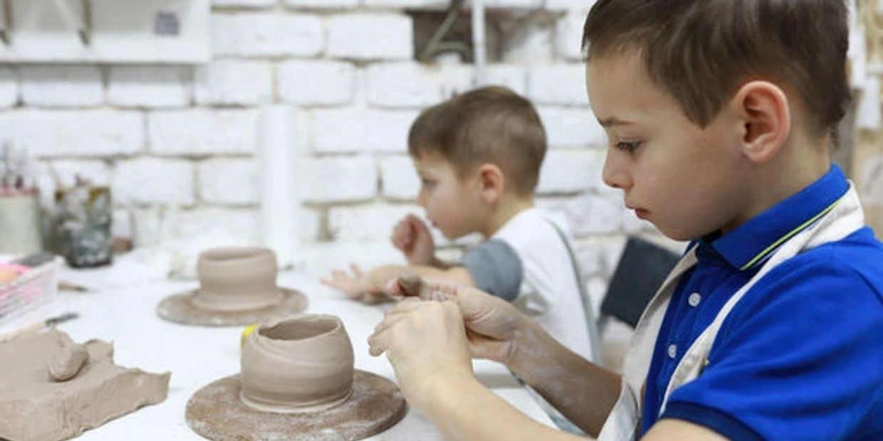 Two young boys sit next to each other and work with clay. Both boys are completing bowls.