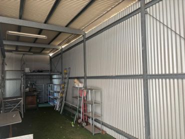 Empty metal storage shed with shelves and ladder inside.