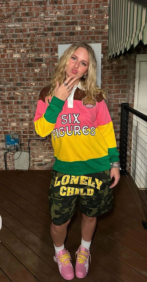 Young woman in colorful casual outfit posing on a porch with brick wall background.