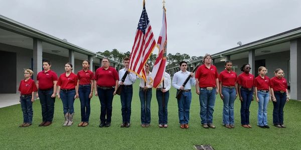 Group of students in red shirts and jeans holding flags in formation outdoors.