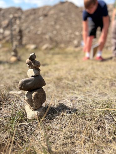 A small stack of balanced stones in the grass with a blurred person in the background.