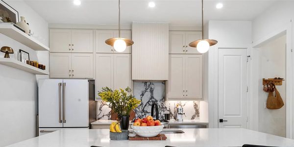 Modern white kitchen with marble backsplash and pendant lights.