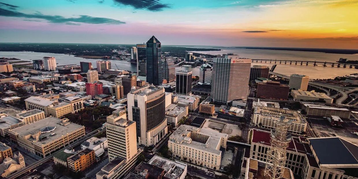 Aerial view of a city skyline at sunset with a river and bridge.